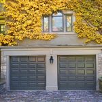 Two blue garage doors set in a building covered in yellow ivy leaves