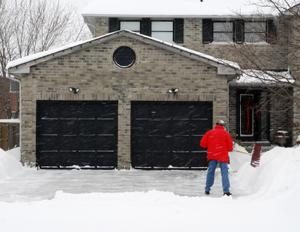 man in red jacket clearing snow outside a double garage
