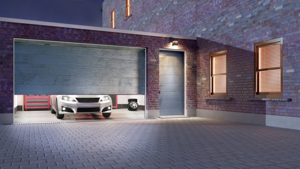 Modern, grey garage door opening at night with silver car waiting with headlights on