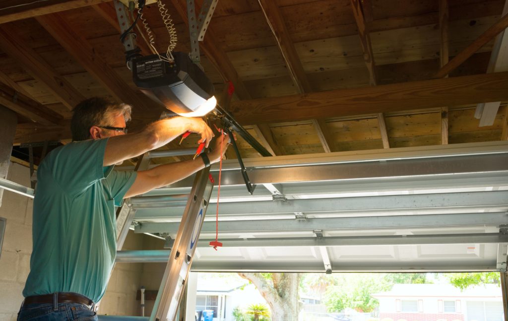 Man up a ladder installing automatic garage door motor