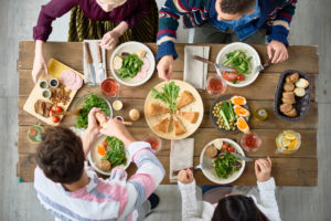 Four people siting around a wooden table covered with dishes of bright, fresh & healthy food
