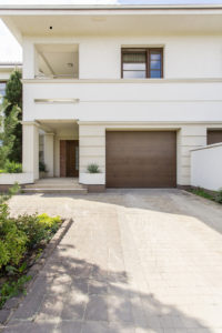 Modern white stone home with long driveway, brown garage door