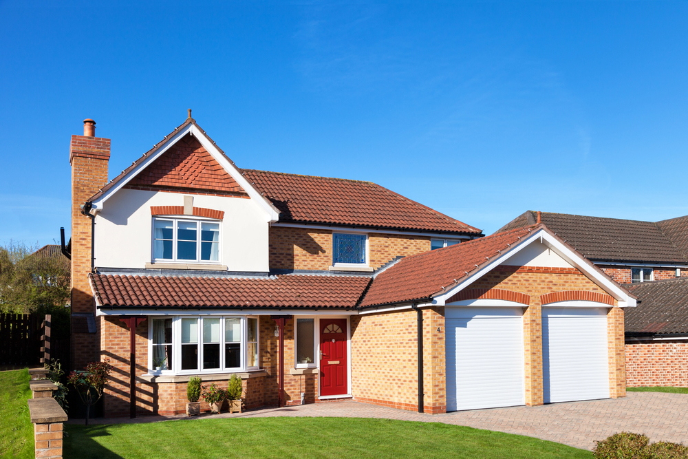 New build detached family home in the UK with brick exterior, red front door, integral double garage and block paved driveway