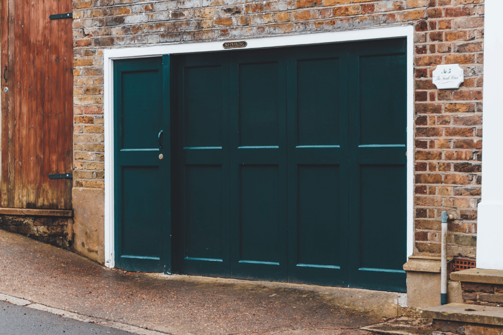 Dark green panelled garage door set within a brick building on a sloped driveway.